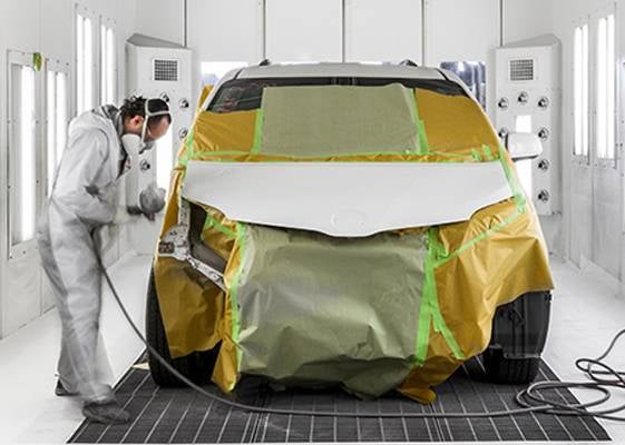 Painter in white suit spraying car in paint booth