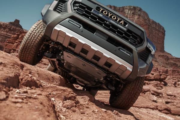 Photo taken at a low angle of a gray Toyota truck peaking over a desert rock